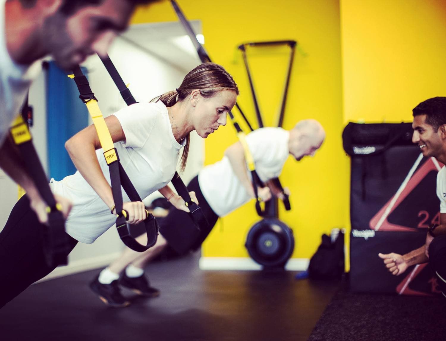 A line of clients rowing on TRX straps under a coach's eye